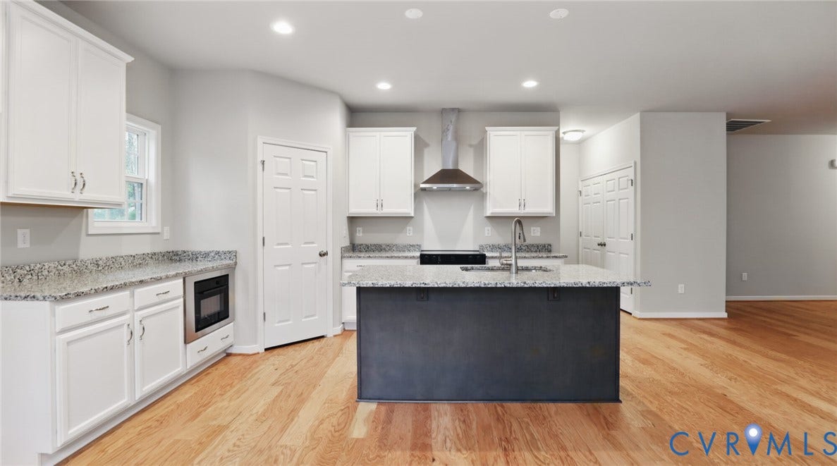 Kitchen featuring wood-finish flooring, white cabinetry, speckled countertops, stainless steel appliances, and a central island with an integrated sink