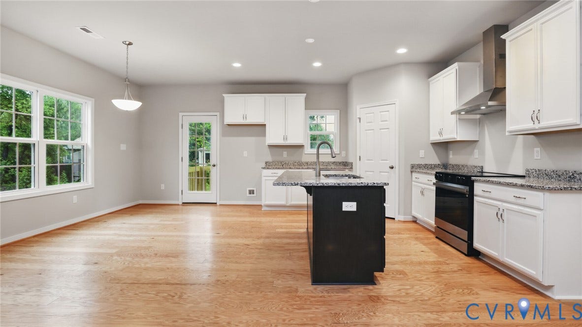 Open-concept kitchen featuring wood-finish flooring, white cabinetry, dark-finish island, and stainless steel appliances