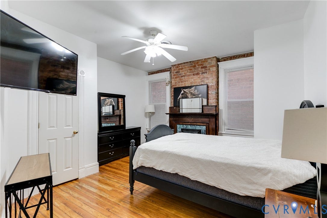 2523 W Main Street, The Fan, Richmond, VA 23220 Exposed brick accent wall, wood-finish flooring, ceiling fan, white paneled door, and a built-in fireplace with a wooden mantel