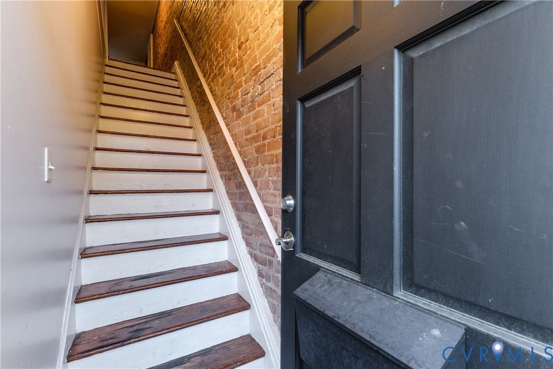 2523 W Main Street, The Fan, Richmond, VA 23220 Staircase featuring wood-finish treads and white risers, accompanied by an exposed brick wall