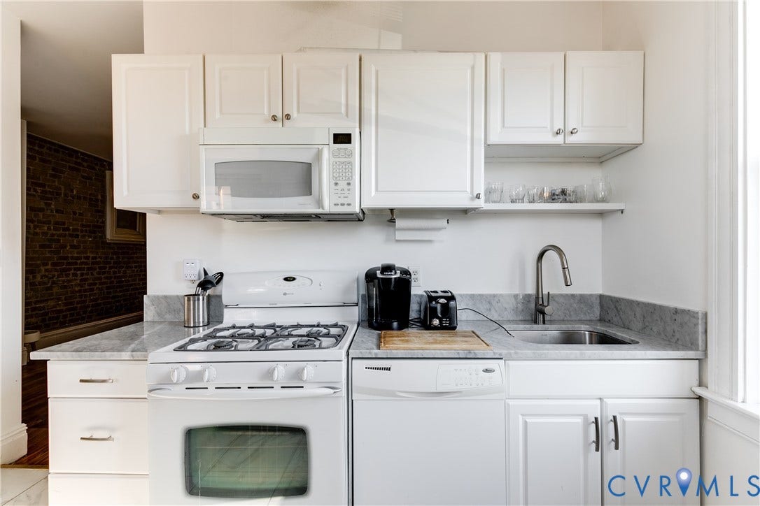 2523 W Main Street, The Fan, Richmond, VA 23220 White cabinetry with polished hardware, stainless steel sink with a gooseneck faucet, light-toned stone countertops, built-in microwave, and a gas range