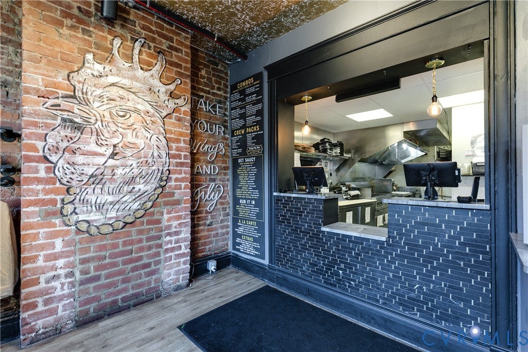 2523 W Main Street, The Fan, Richmond, VA 23220 Brick wall with graphic art, wood-finish flooring, dark subway tile accent, serving window, and commercial kitchen equipment