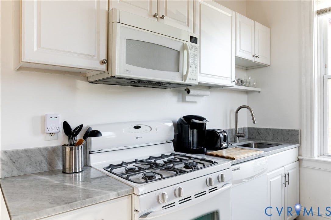 2523 W Main Street, The Fan, Richmond, VA 23220 White cabinetry with silver hardware, stone countertops with a matching backsplash, stainless steel sink with a high-arc faucet, white oven with gas burners, and an over-the-range microwave