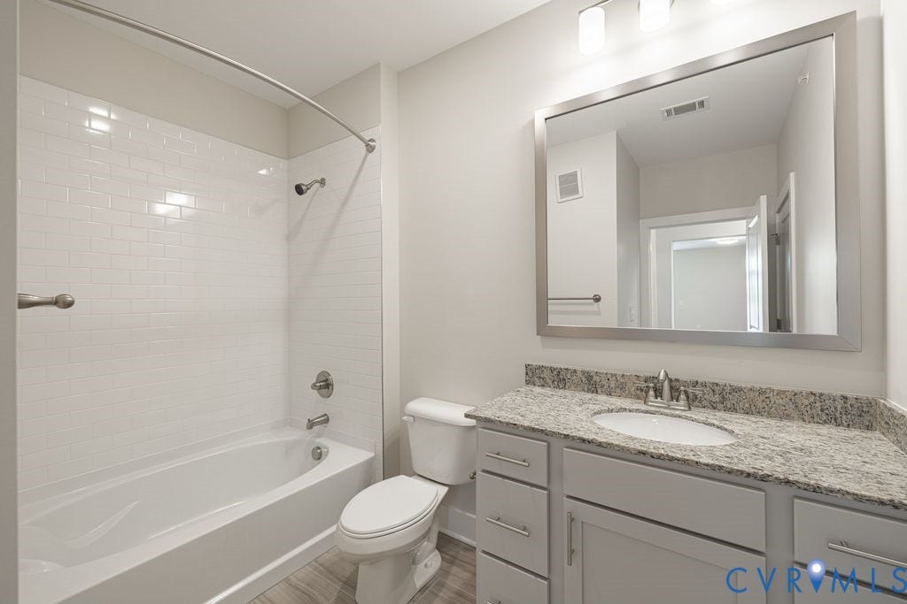 10530 Stony Bluff Drive, #102, Stony Run Condos, Ashland, VA 23005 Bathroom featuring a built-in tub with white subway tile surround, a single vanity with a light-colored countertop, and wood-finish flooring