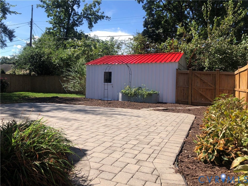 4919 Park Avenue, Near West End, Richmond, VA 23226 Paver patio with a decorative border, a white storage shed with a red metal roof, garden beds, and wood privacy fencing.