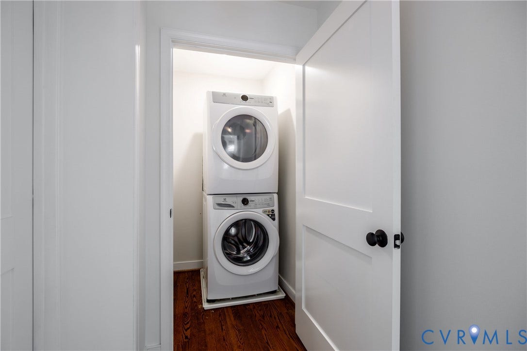 4919 Park Avenue, Near West End, Richmond, VA 23226 Stackable washer and dryer appliances within a dedicated closet, featuring a paneled door and dark wood-finish flooring