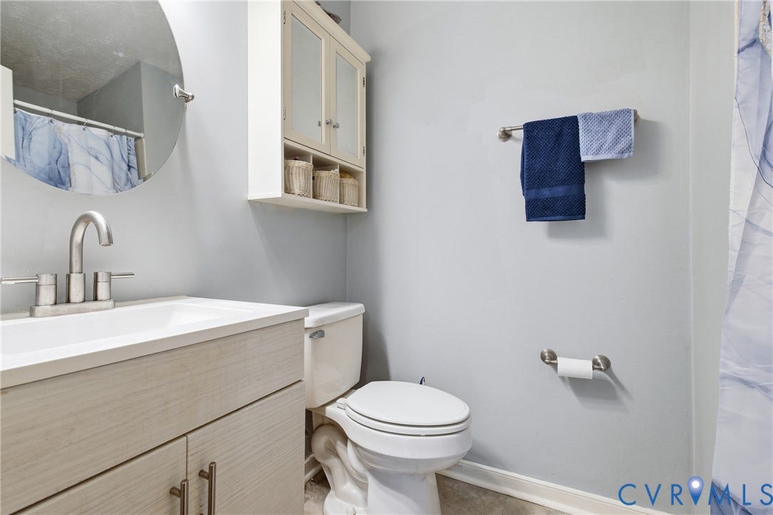 Bathroom featuring a light-toned vanity with brushed nickel hardware, a white integrated sink, and a circular mirror and fiberglass shower