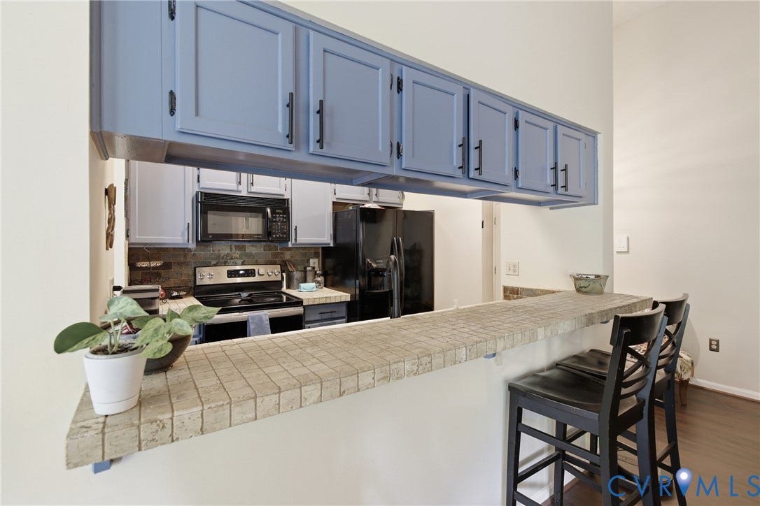 Kitchen pass-through with tile-finished breakfast bar, overhead cabinetry