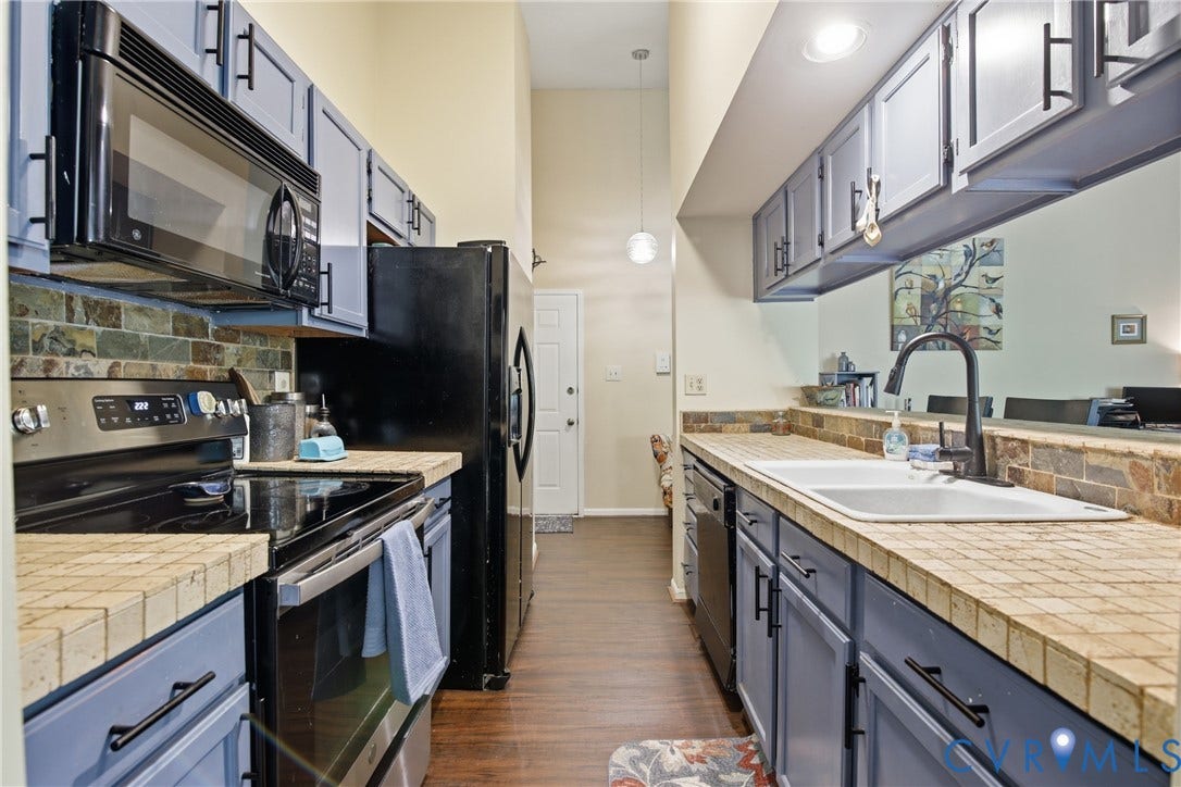 Kitchen featuring blue cabinetry, black appliances, tile countertops, and a stone backsplash