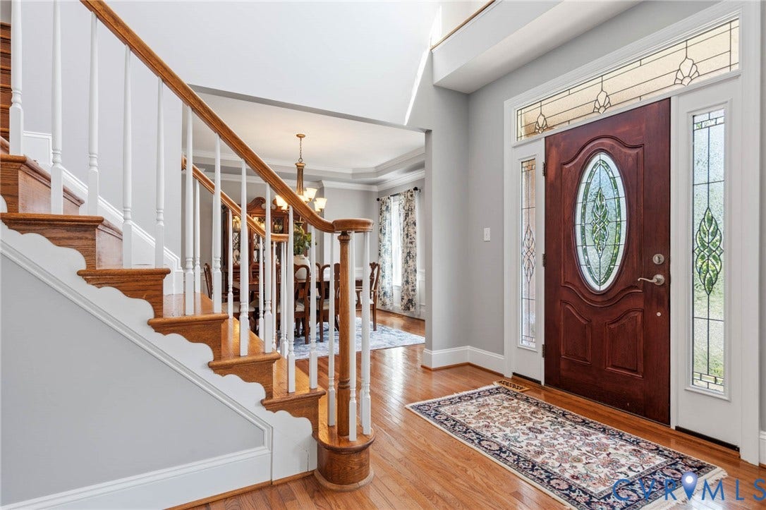 Wood-finish flooring, staircase with white risers and wood-finish railing, and a front entry door with leaded glass panels