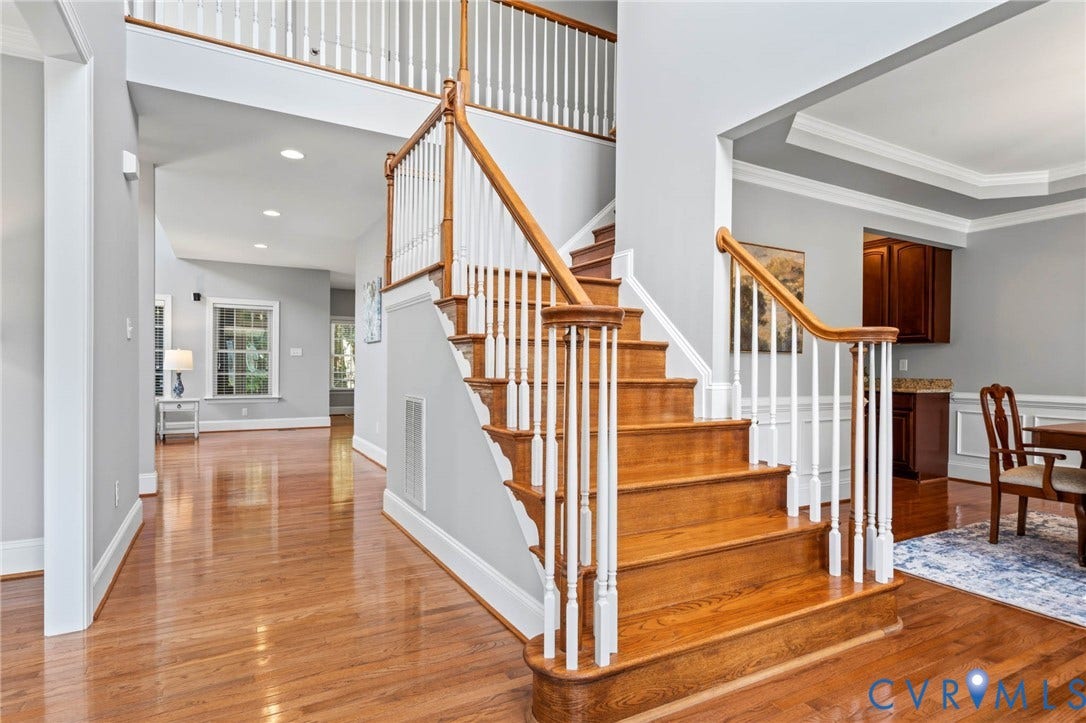 Hardwood flooring, wood staircase with white risers and balusters, tray ceiling, recessed lighting, and crown molding