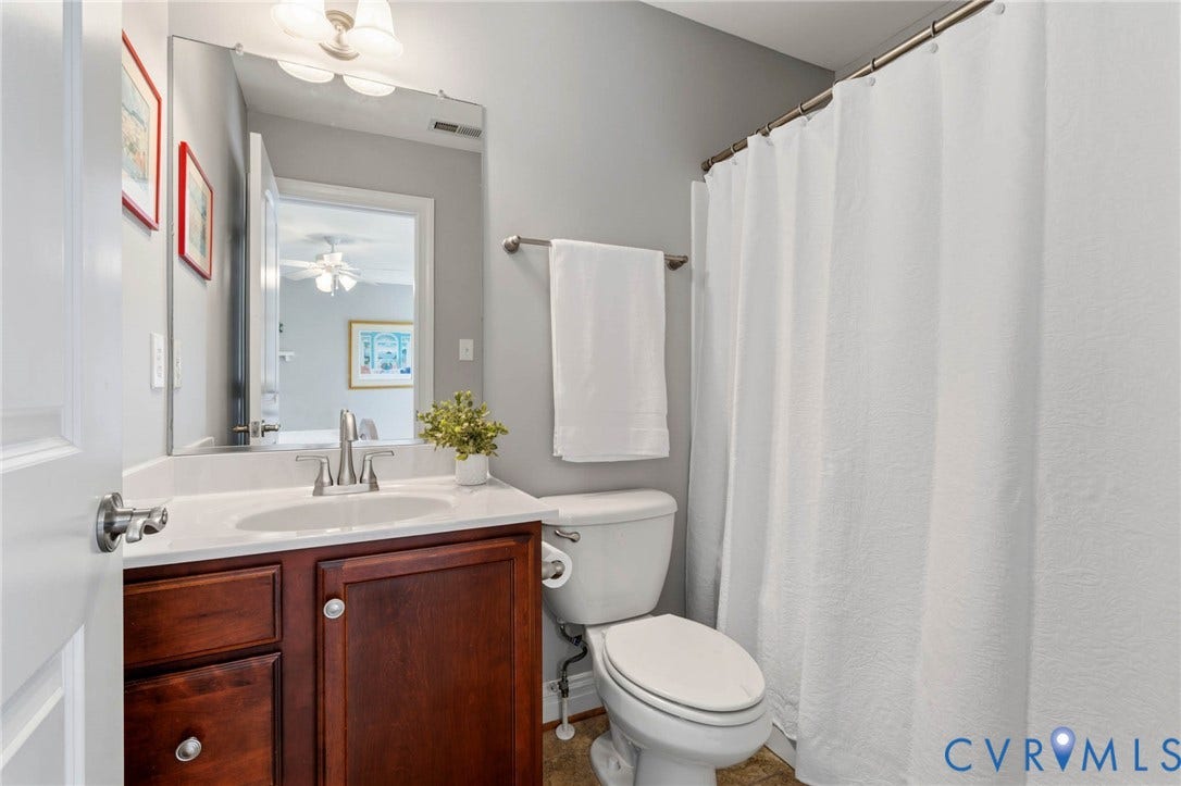 Bathroom featuring a wood-finish vanity with a white countertop, wall-mounted mirror, and a full shower with a white curtain