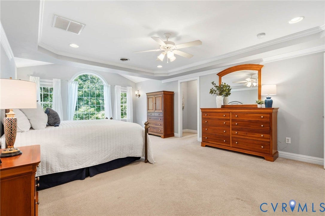 Tray ceiling with recessed lighting, ceiling fan, arched window, and sconce lighting