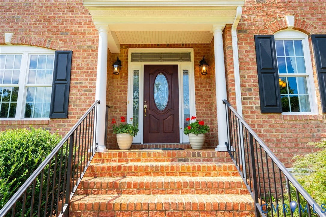 Brick facade with a covered entry, featuring a decorative front door with side lights and transom window
