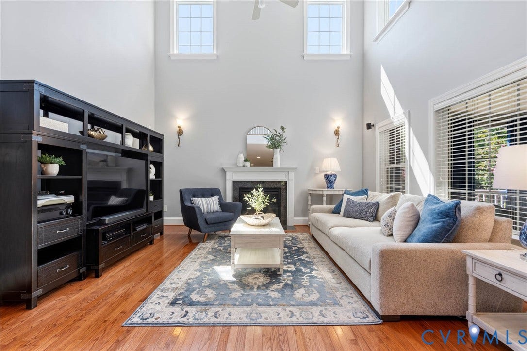 Two-story living room featuring hardwood flooring, a fireplace with a mantel, and high windows