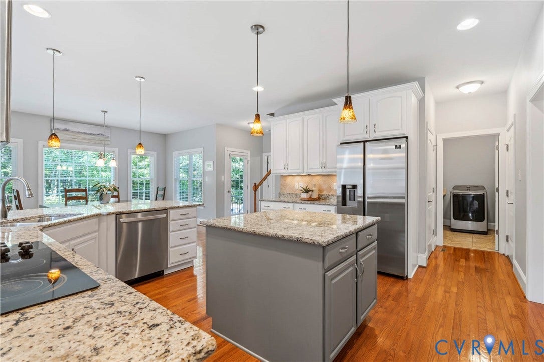 Kitchen featuring light-toned cabinetry, granite countertops, stainless steel appliances, a center island, and wood-finish flooring