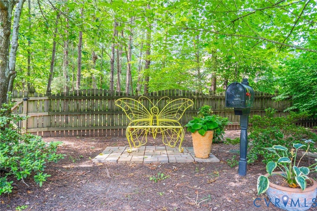 Fenced backyard featuring mature trees, a decorative mailbox, and a paver stone seating area