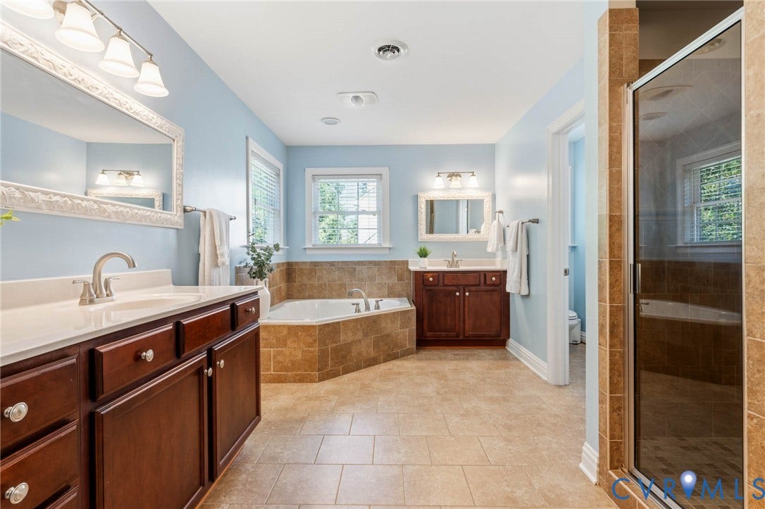 Dual vanity sinks with white countertops, corner soaking tub, separate glass-enclosed shower, and tile flooring