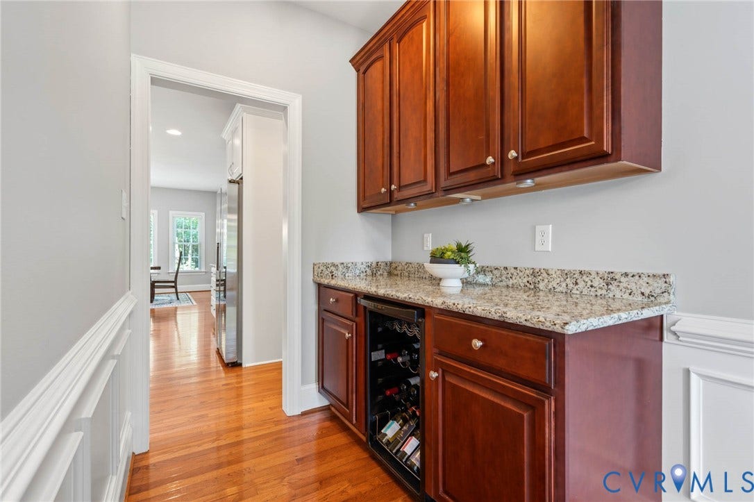 Hardwood flooring, wood cabinetry with upper and lower storage, stone countertop, integrated beverage cooler, and wainscoting