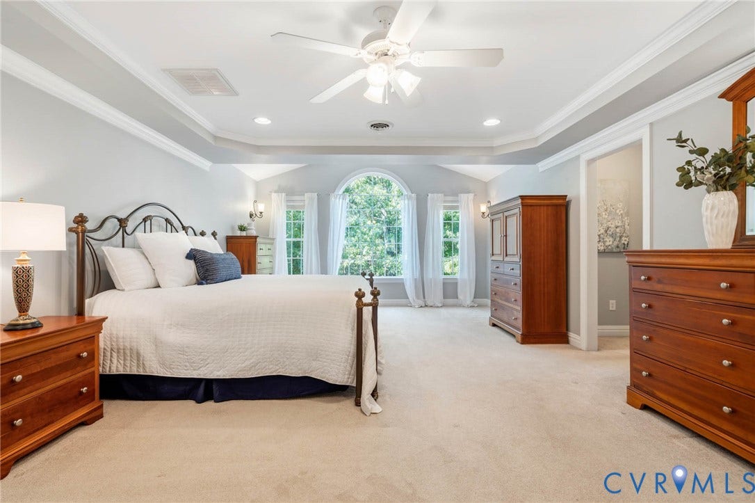 Tray ceiling with crown molding, recessed lighting, ceiling fan, arched window, and carpet flooring