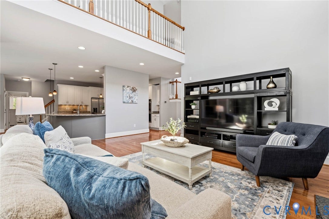 Two-story living area featuring hardwood flooring, a mezzanine with white balusters, and a kitchen with white cabinetry, granite-style countertops, and pendant lighting
