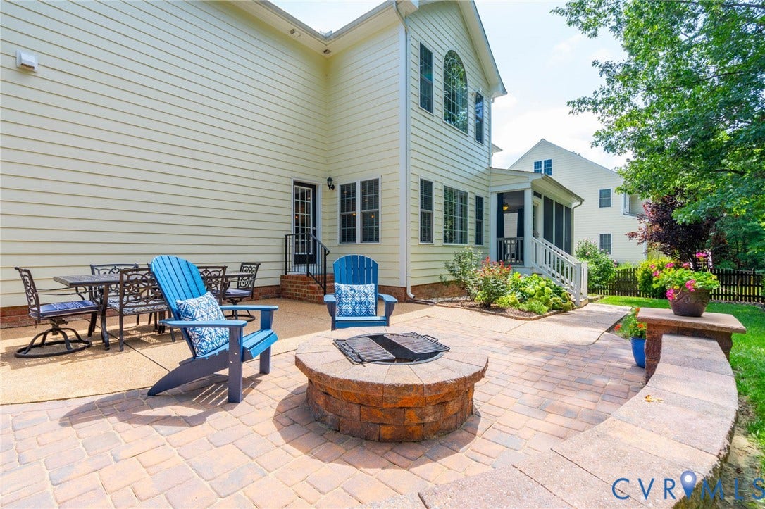 Expansive paver patio with a built-in fire pit, stone retaining wall, and screened porch access