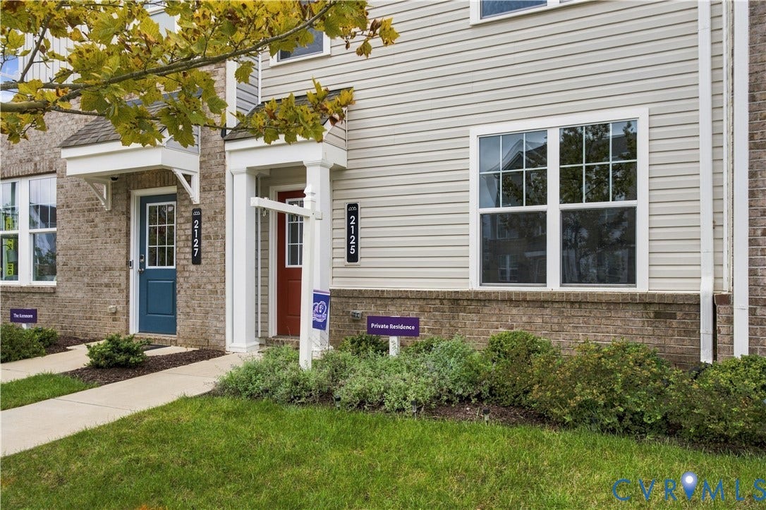 Exterior facade featuring brick and horizontal siding, individual entry doors with overhangs, and a well-maintained lawn