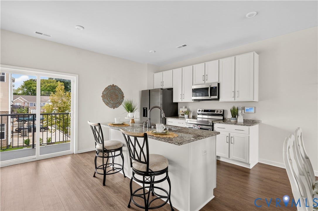 Kitchen featuring a central island with countertop seating, white cabinetry, integrated stainless steel appliances, and wood-finish flooring