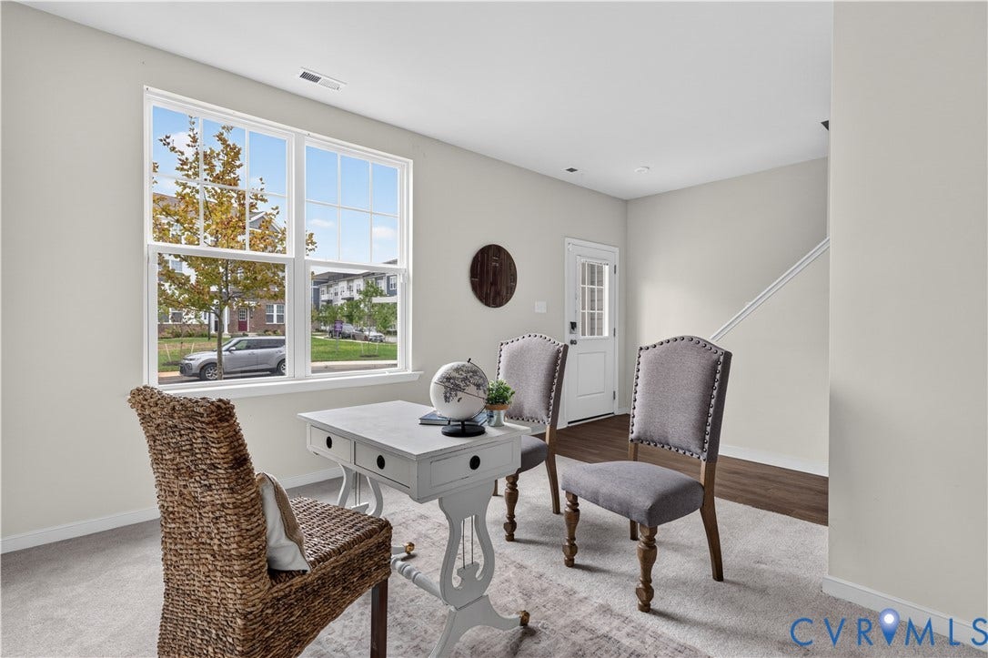 Light-toned walls, large window with multi-pane design, wood-finish flooring, white door with glass panels, and carpeted area