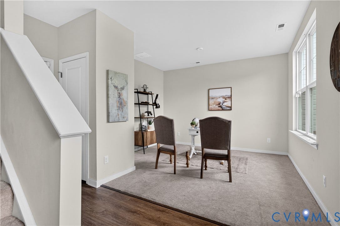 Carpeted room with a large window and wood-finish flooring at the entry