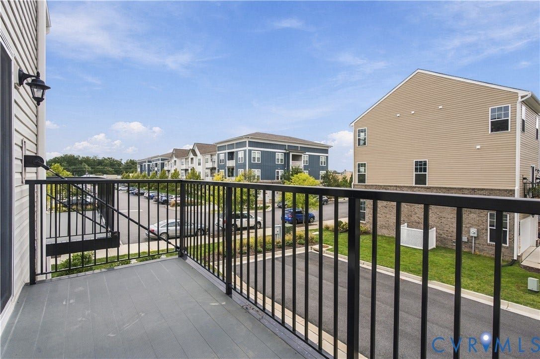 Balcony with black metal railing, gray plank flooring, and an exterior wall light fixture