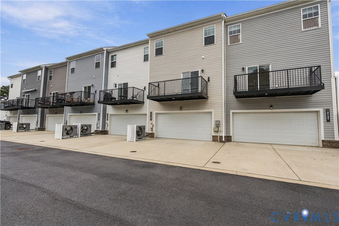 Siding exterior in a neutral tone, featuring a private balcony with black railings, ground-level garage, and a concrete driveway