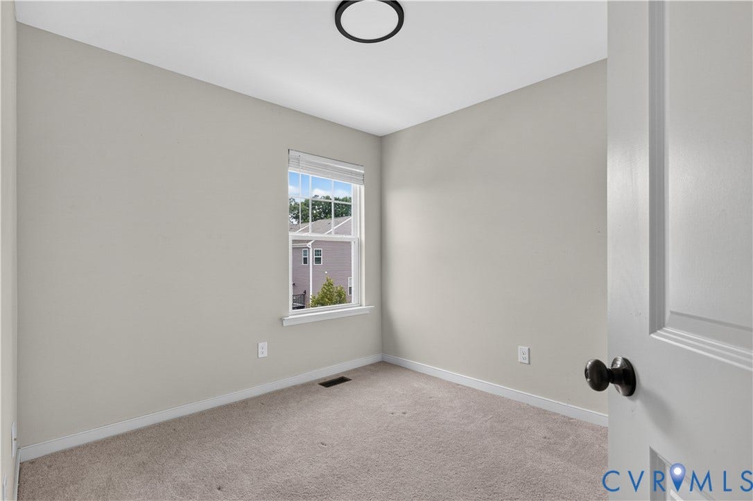 Neutral wall tones with a single window featuring blinds, carpeted flooring, and a ceiling-mounted light fixture