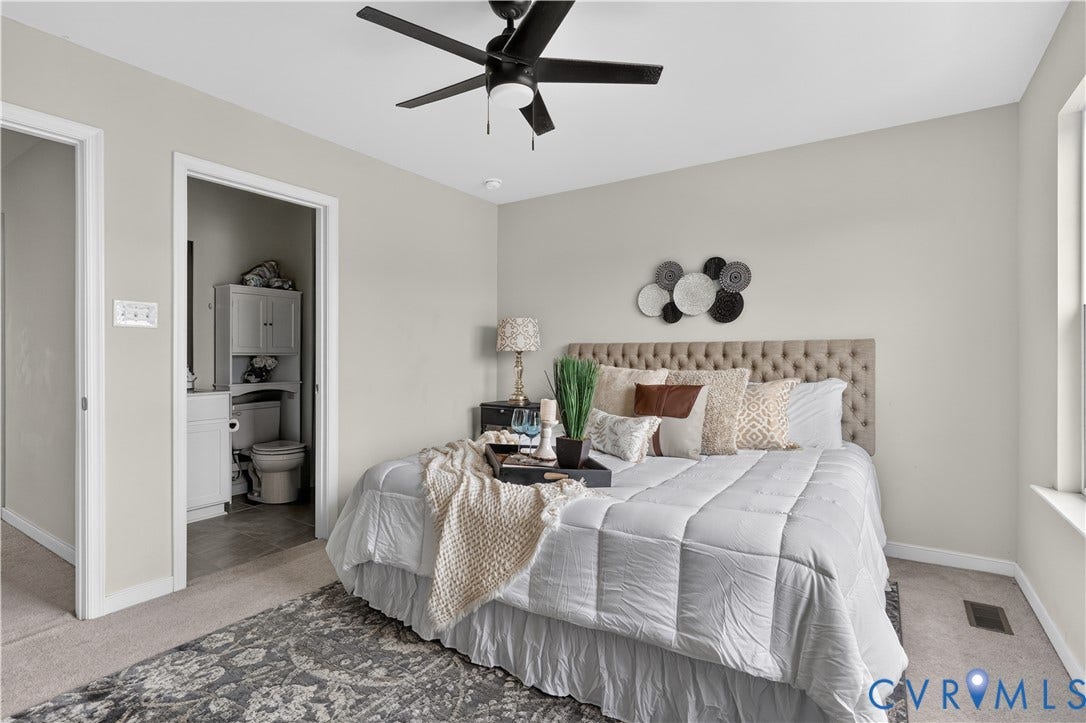 Neutral wall color, ceiling fan with integrated lighting, carpeted flooring, and an adjoining bathroom with built-in cabinetry