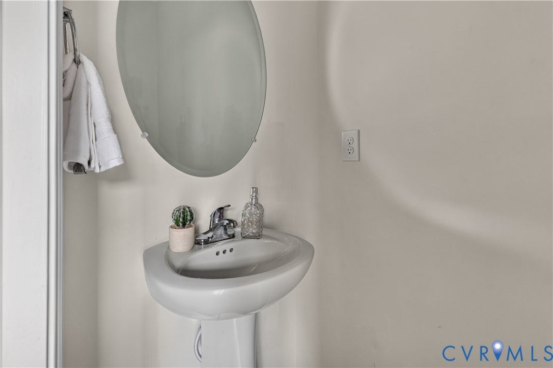 Pedestal sink with a chrome faucet, oval wall mirror, and wall-mounted towel rack