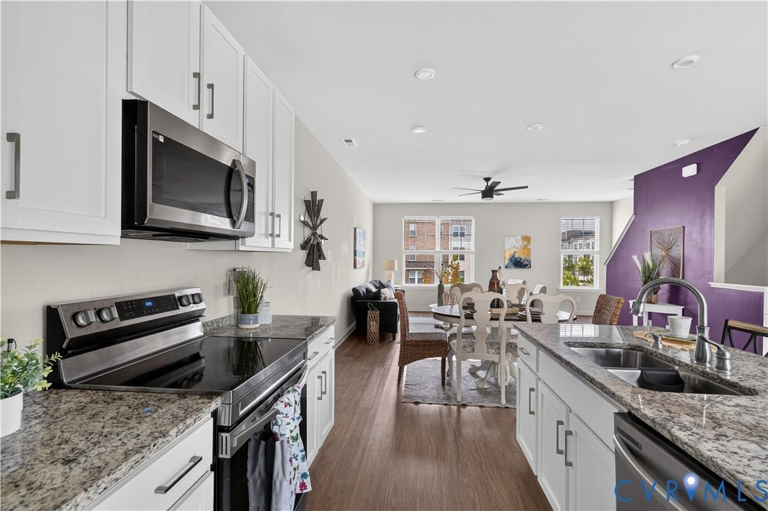 Open-concept kitchen featuring white cabinetry, stainless steel appliances, granite countertops, and wood-finish flooring