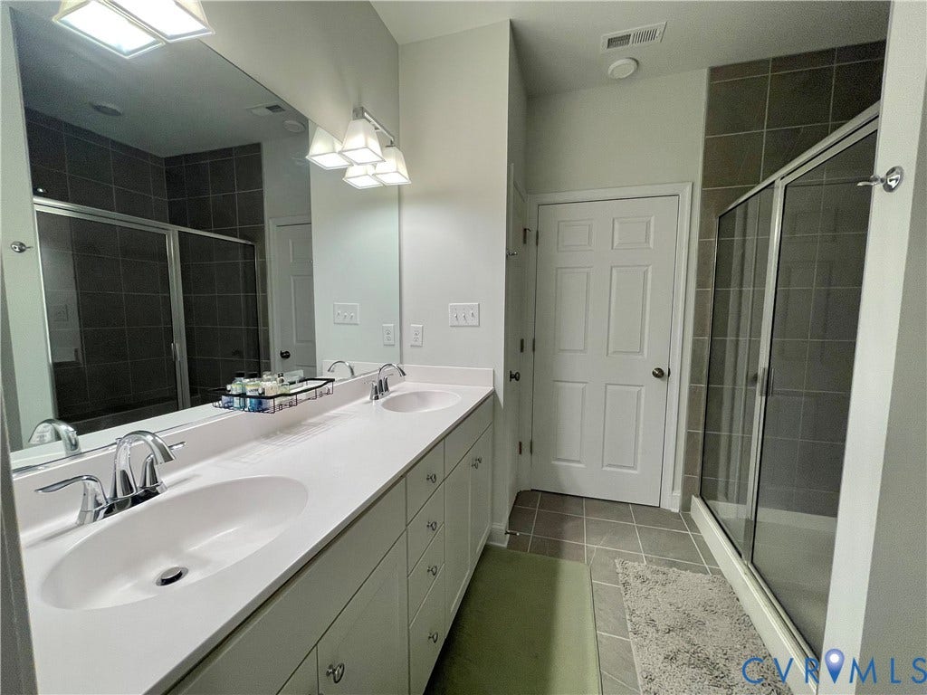 6905 Leire Lane, Chesterfield, VA 23832 Dual vanity with undermount sinks and chrome fixtures, expansive wall mirror, tile flooring, glass-enclosed shower with tile surround, and overhead lighting