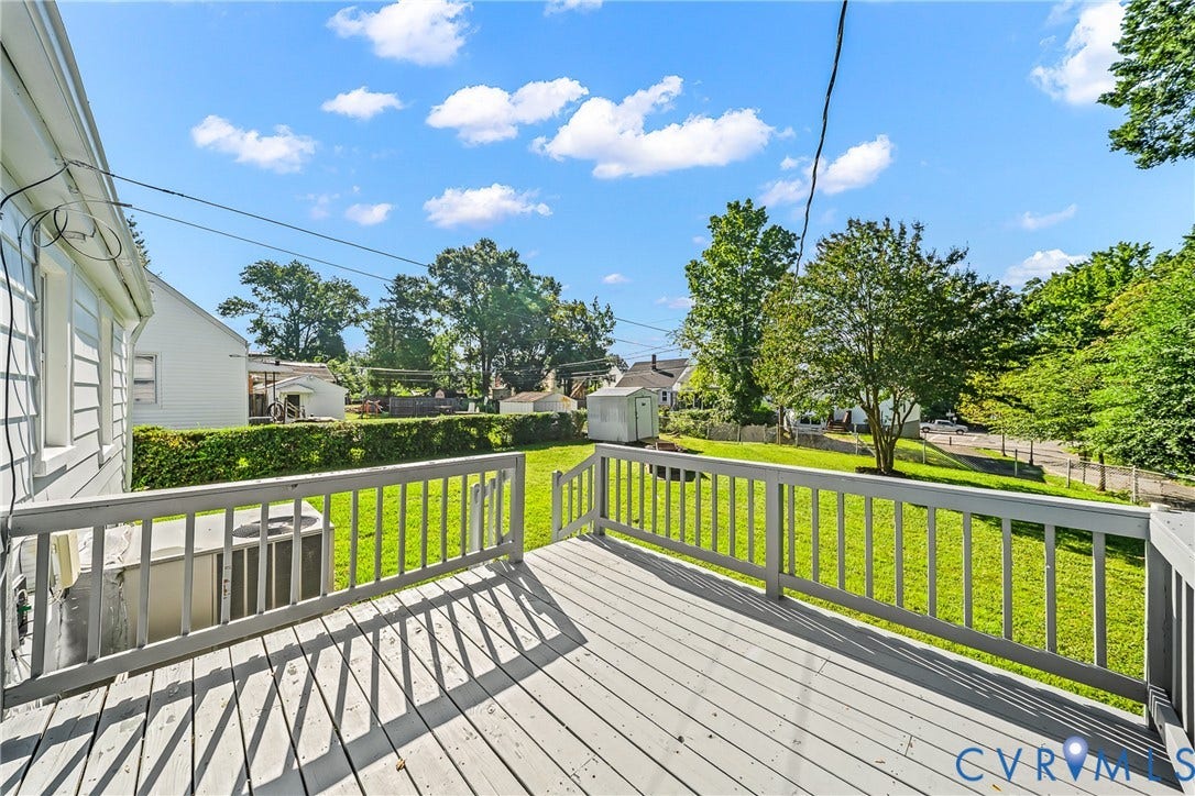Outdoor deck with painted railing and wood-finish flooring overlooking a manicured lawn