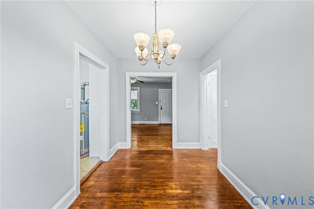 Hallway featuring wood-finish flooring, light gray walls, white trim, and a bronze-finish chandelier with frosted glass shades
