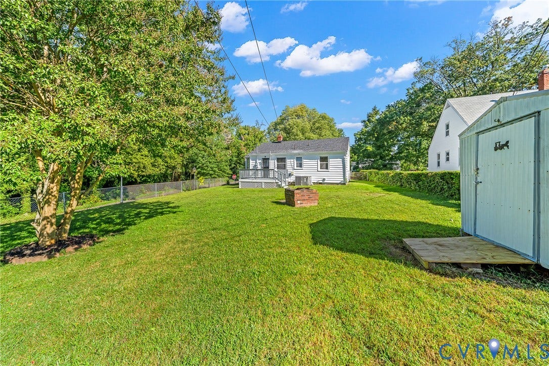 Expansive grassy yard featuring mature trees, a detached storage shed, and a brick fire pit