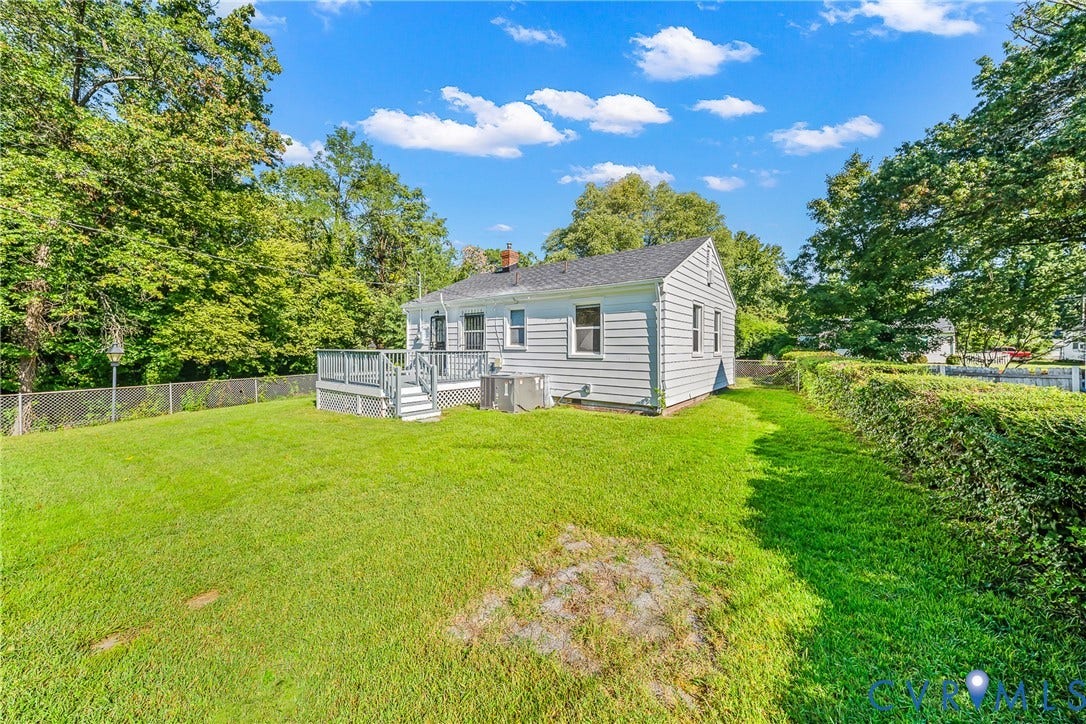 Expansive backyard with a manicured lawn, an elevated deck, and mature perimeter trees