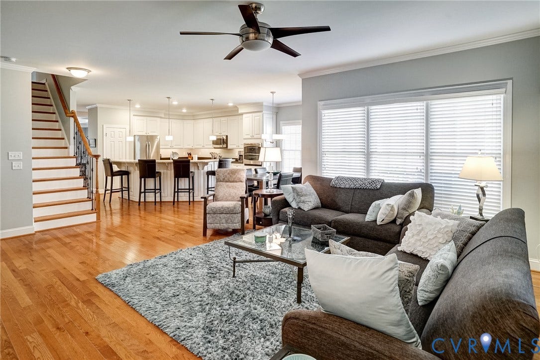 4938 Grey Oaks Villas Drive, Glen Allen, VA 23059 Hardwood flooring throughout, a staircase with wood treads and a wrought iron baluster, a kitchen with white cabinetry and an integrated island, and a ceiling fan with dark wood-finish blades