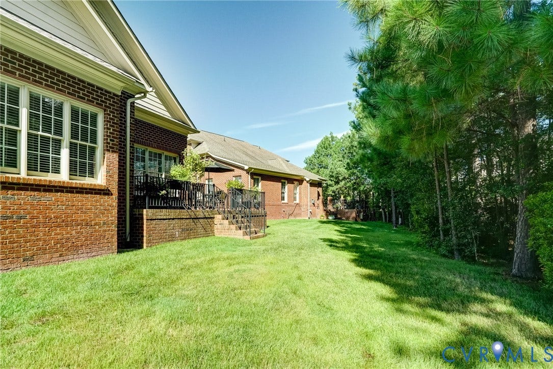 4938 Grey Oaks Villas Drive, Glen Allen, VA 23059 Expansive lawn with mature trees and a brick exterior, featuring multiple windows with louvered shutters and a raised patio with metal railings