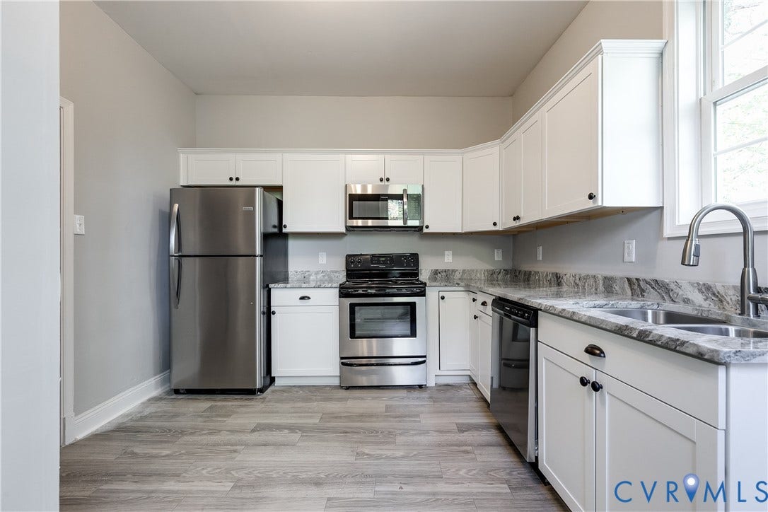 Kitchen featuring white shaker-style cabinetry, stainless steel appliances, speckled countertops, and wood-finish flooring