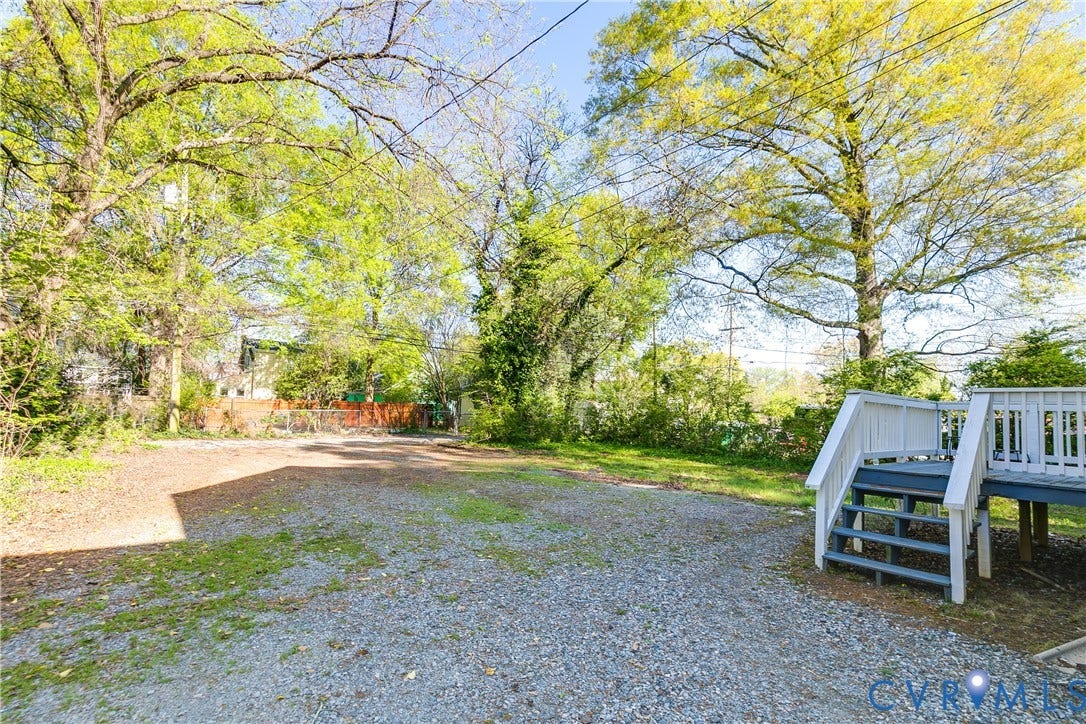 Spacious gravel area, elevated wood deck with white railings, mature trees, and natural landscaping