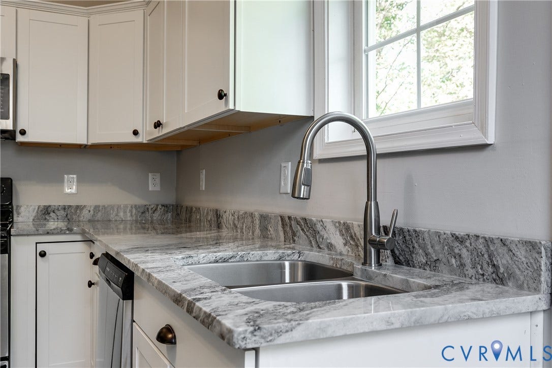 White shaker-style cabinetry with dark hardware, stainless steel gooseneck faucet, double basin stainless steel sink, and light-toned countertops