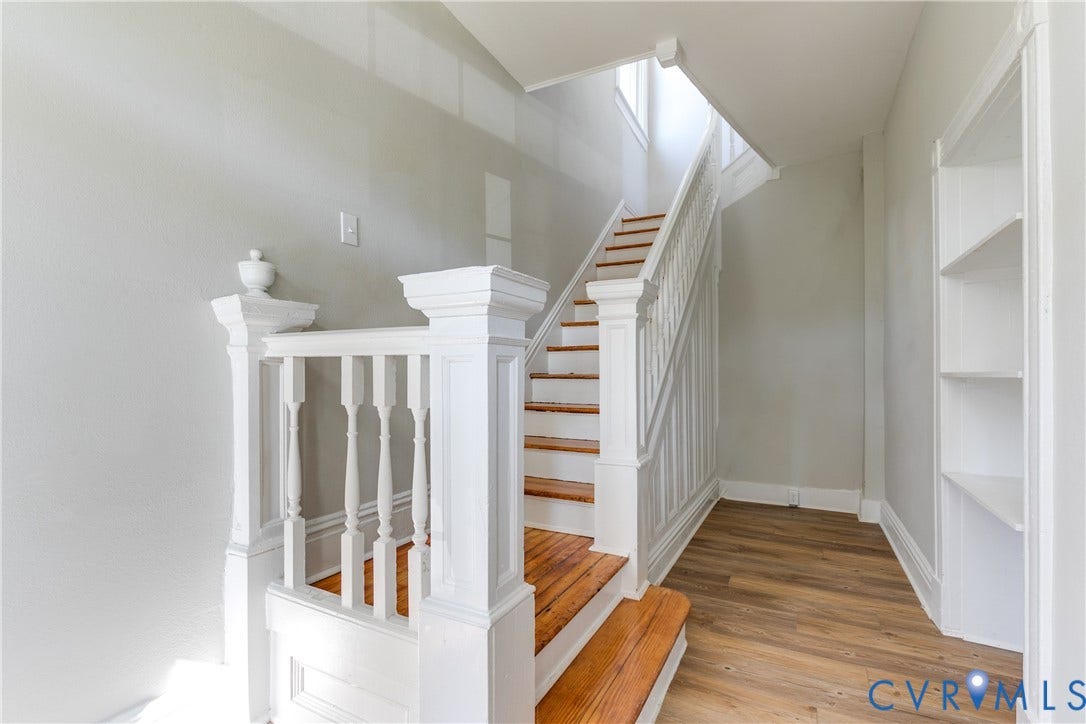 Wood-finish flooring, white painted staircase, wood treads, white painted built-in shelving, and light gray walls