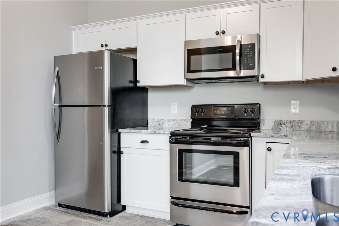 White cabinetry, stainless steel appliances, granite-style countertops, wood-finish flooring, and an over-the-range microwave