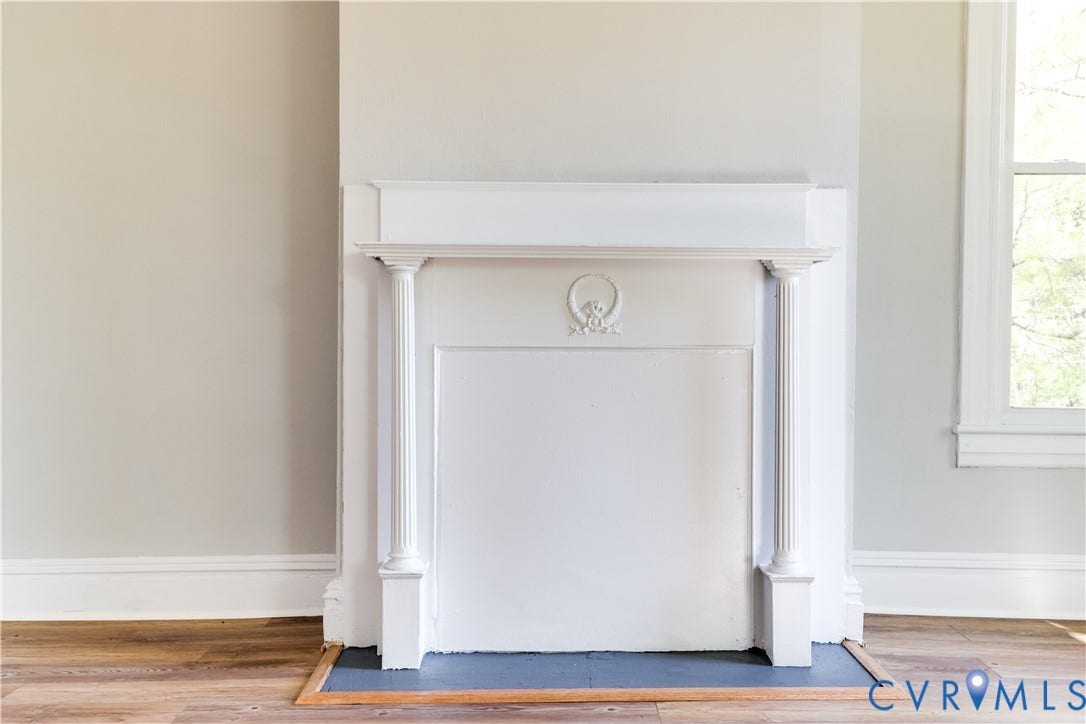 White fireplace mantel with fluted columns and decorative molding, set against light-toned walls with wood-finish flooring