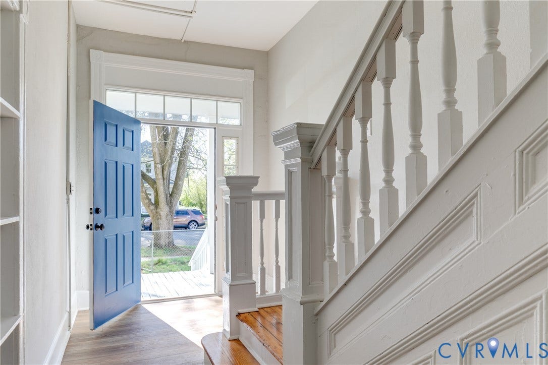 Entryway featuring a paneled door, transom window, wood-finish flooring, and a staircase with a detailed newel post and balusters
